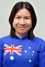 A headshot portrait of Mai Hoang, smiling and looking directly into the camera, wearing a bright blue sweater featuring the Australian flag