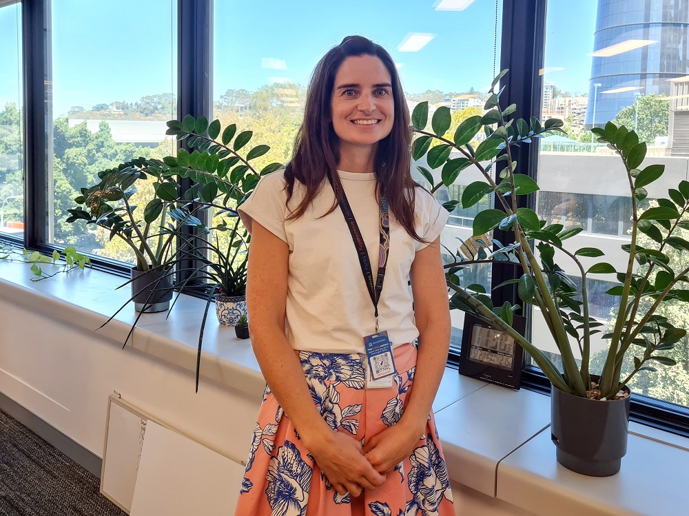 Karen Nitsche, Child and Adolescent Community Health Senior Evaluation and Information Officer, Research and Evaluation team, standing in front of a window, flanked by pot plants