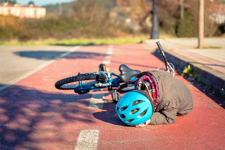 Child with bike helmet lying on the ground following a bike accident