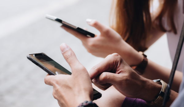 A close up of two pairs of hands. Each person is holding a smart phone and tapping the screens